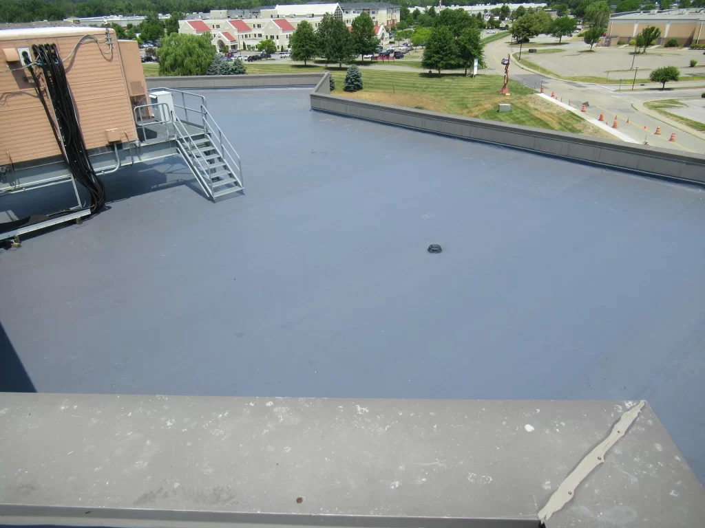Flat commercial roof with a smooth surface and an HVAC unit, overlooking a landscaped area.