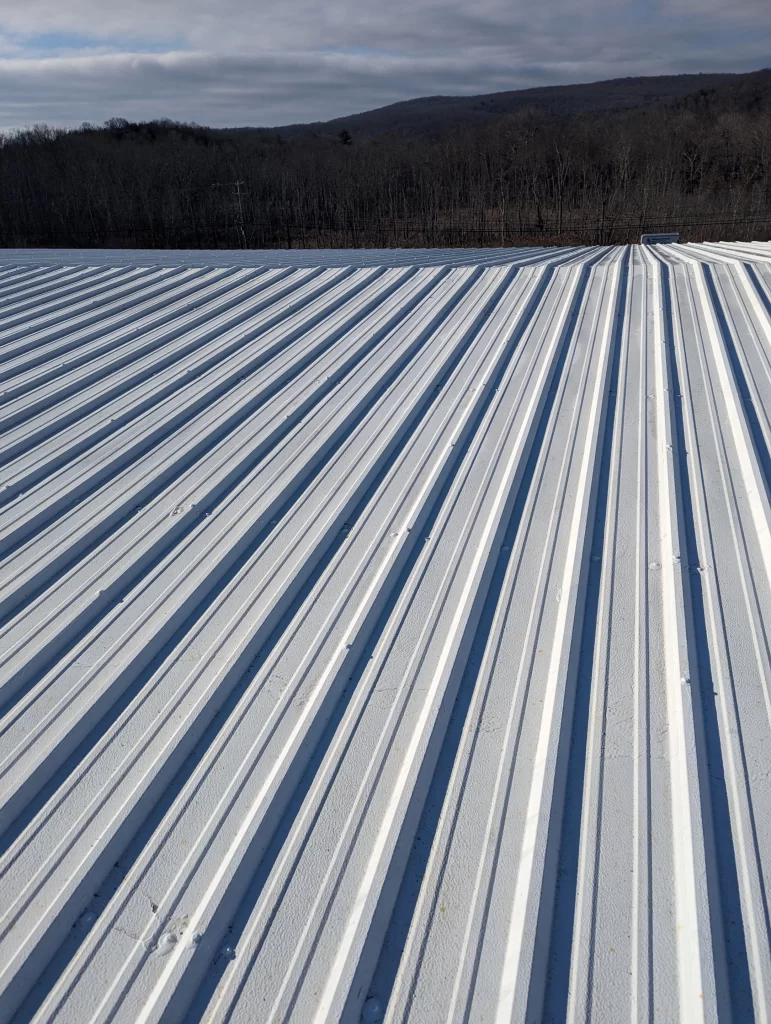 Large white metal roof panels on a commercial building with forested hills in the background