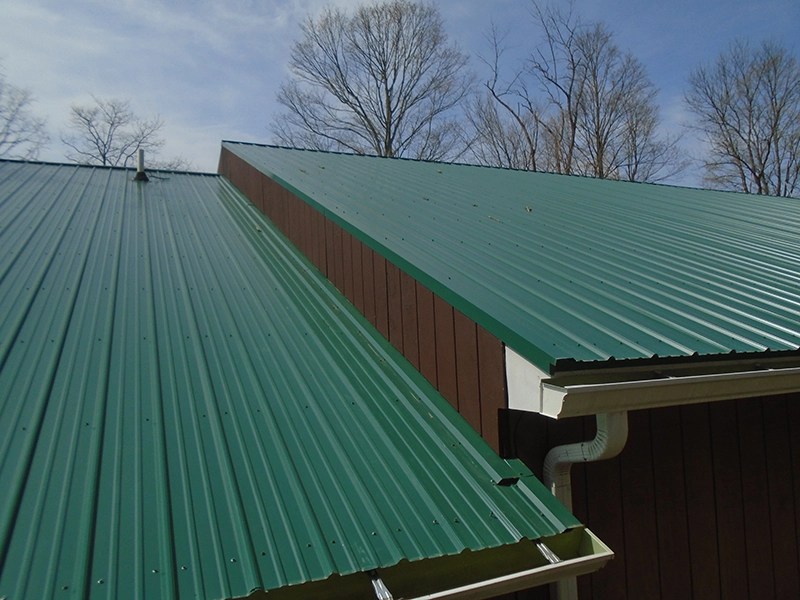 Green metal roofing on a residential building with multiple roof slopes and a gutter system