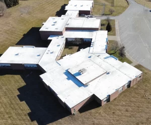 Aerial drone view of large commercial building with white TPO membrane roofing system, showing multiple roof sections and skylights