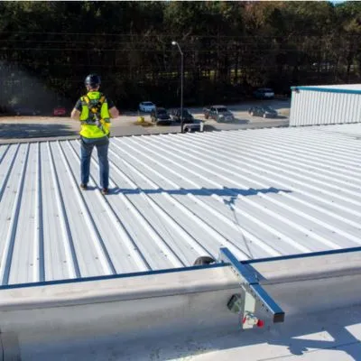 Worker wearing a safety harness and standing on a commercial metal roof with an anchor tie-down system for fall protection